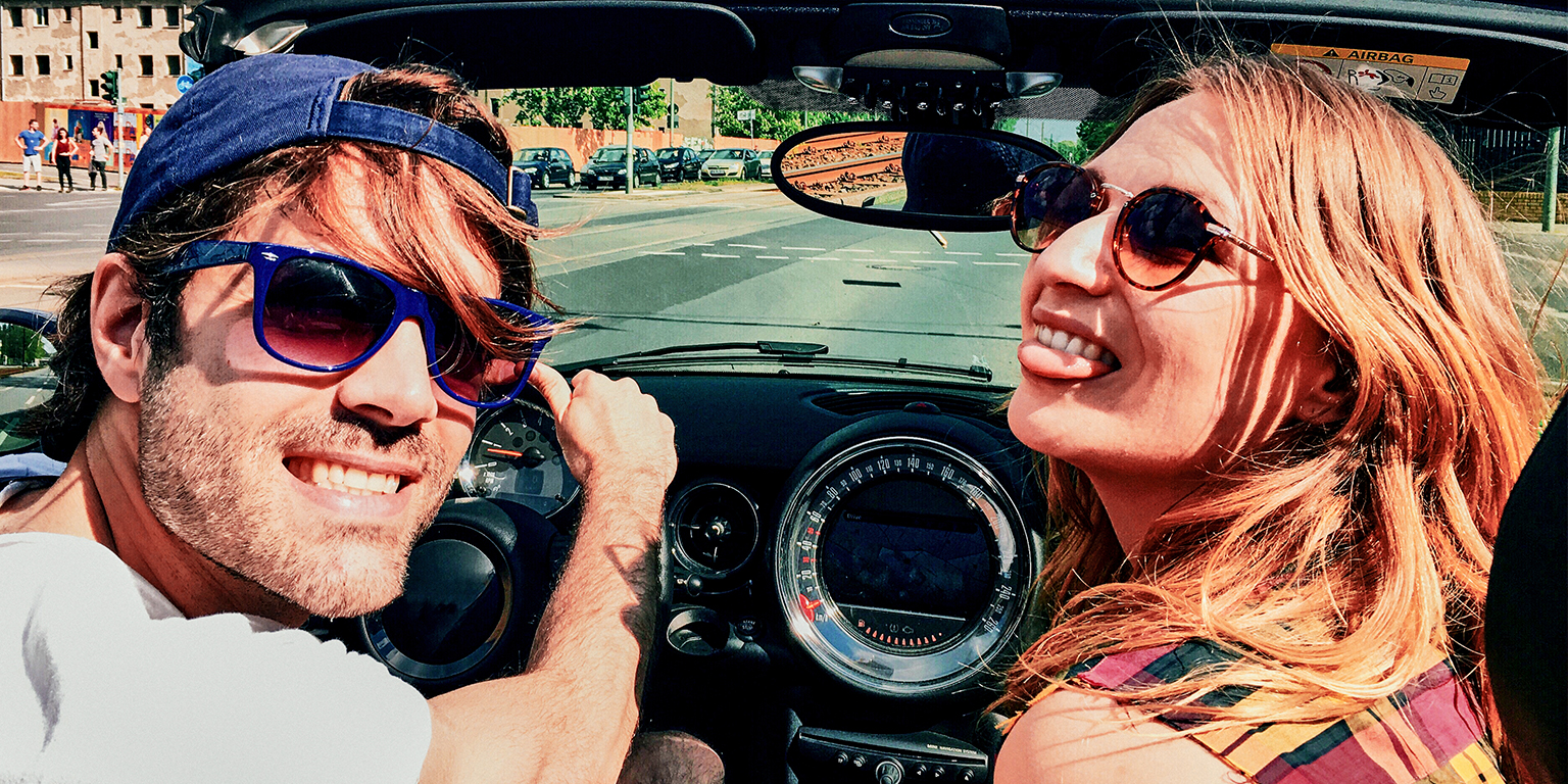 1536X768 Young couple posing for the camera in a convertible car on a sunny day