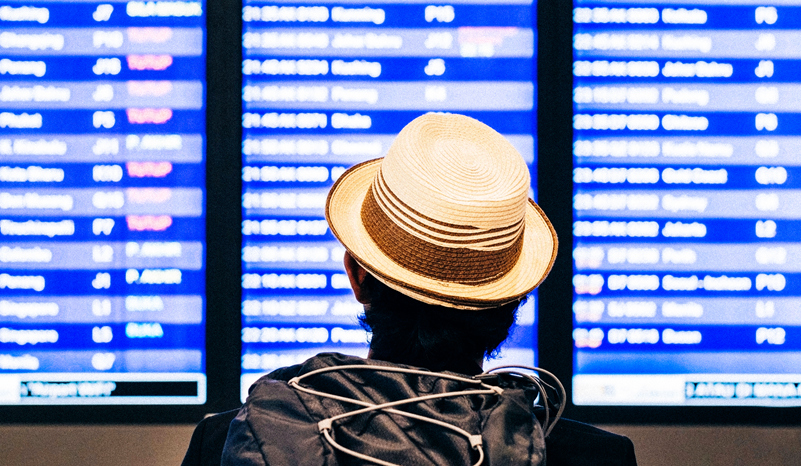 Back view of a man with a hat reading the digital departure flight time boards at the airport