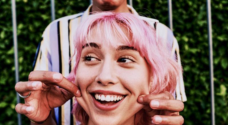 Happy woman with pink hair getting cheeks pinched by friend.