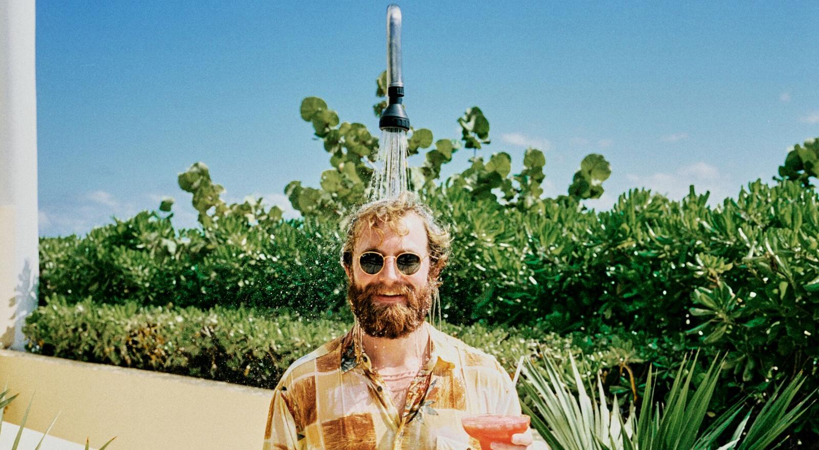 Large Web and Screen A bearded man wearing sunglasses stands under the outdoor shower while holding a cocktail in his hand