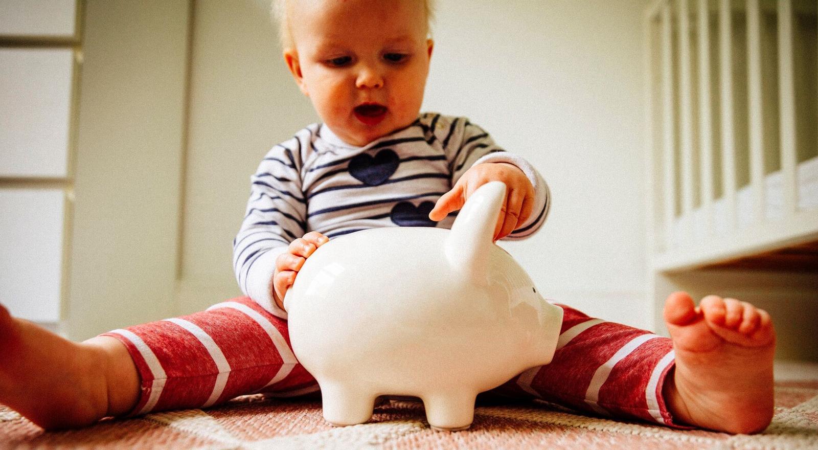 Large Web and Screen A toddler sits on the floor with a piggy bank