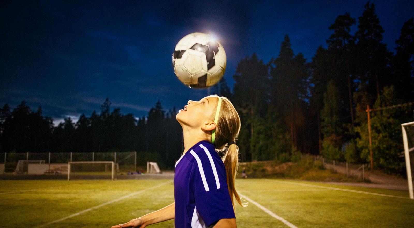Large Web and Screen A young girl works on her heading skills with a ball on a football field at night
