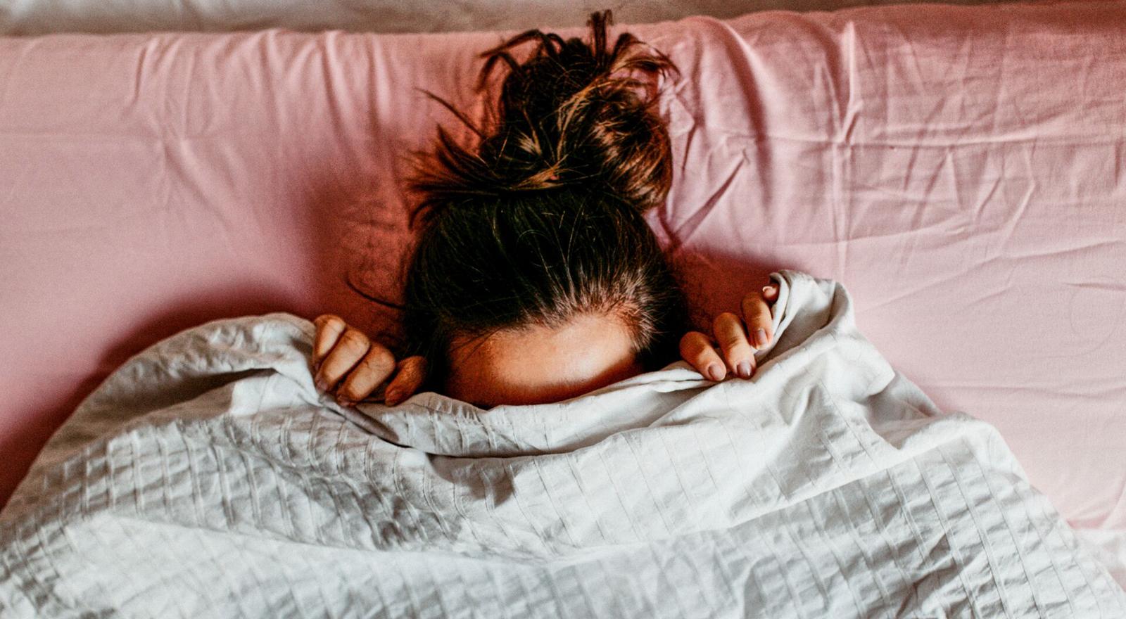 Large Web and Screen Overhead view of a woman laying in bed and hiding her face with a blanket