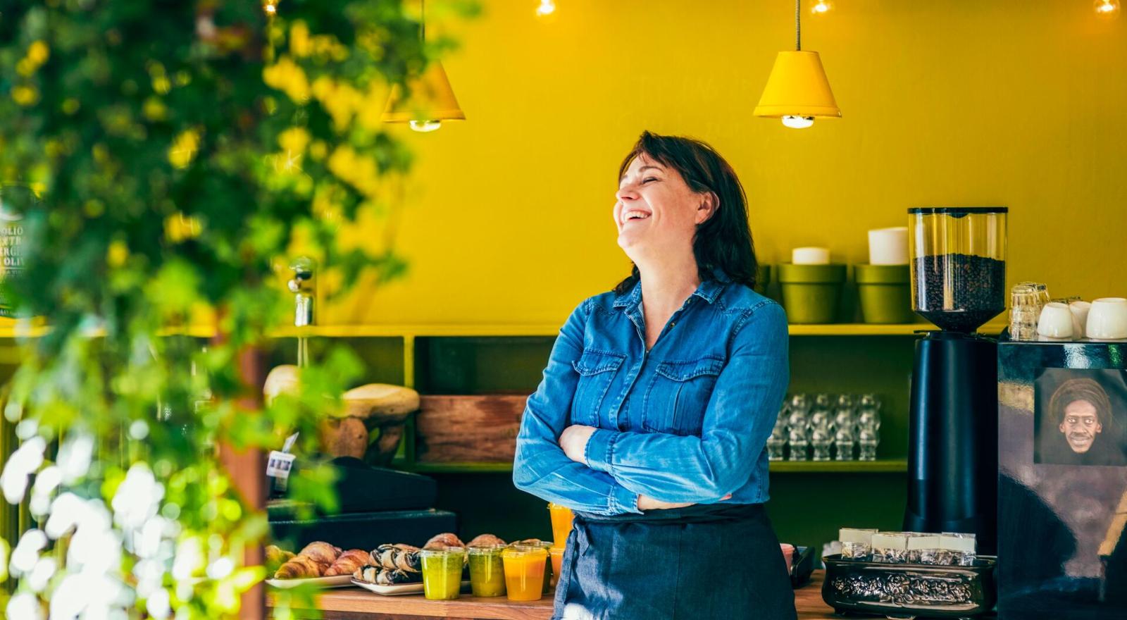 Laughing young woman cafe owner standing by a yellow wall