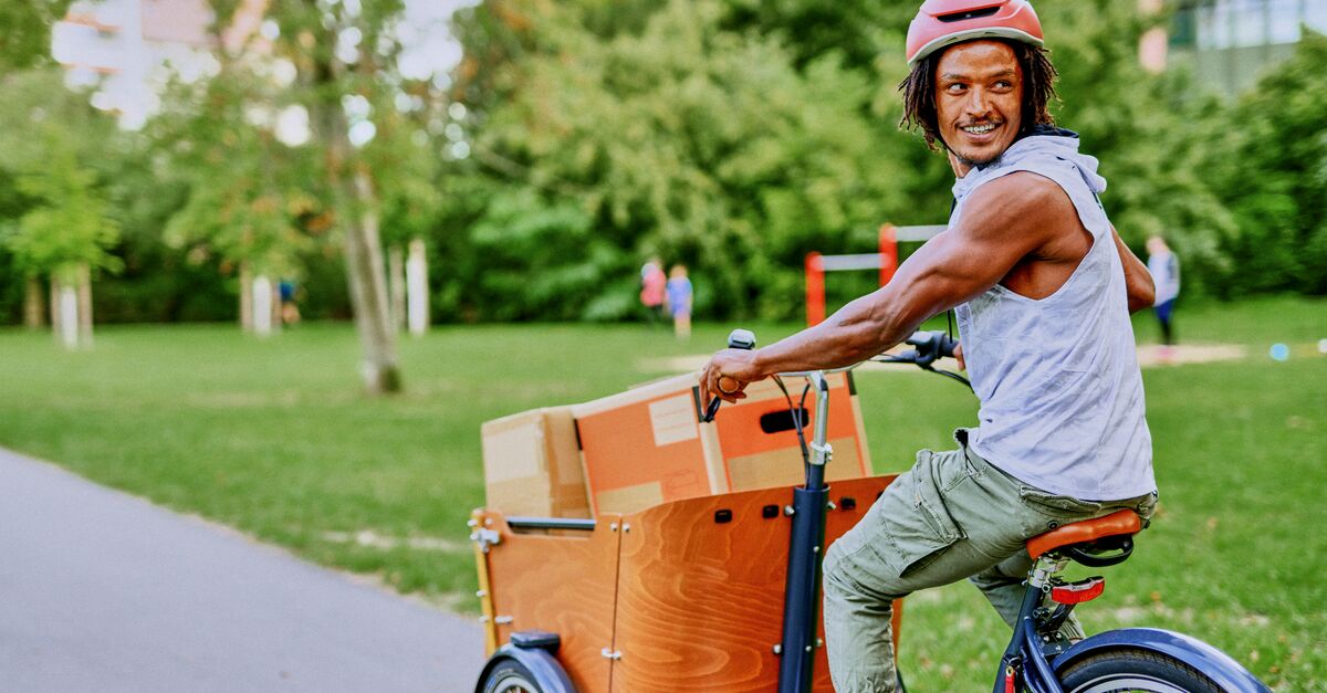 LinkedIn and Facebook Young man cycling through the park on cargo bike delivering packages