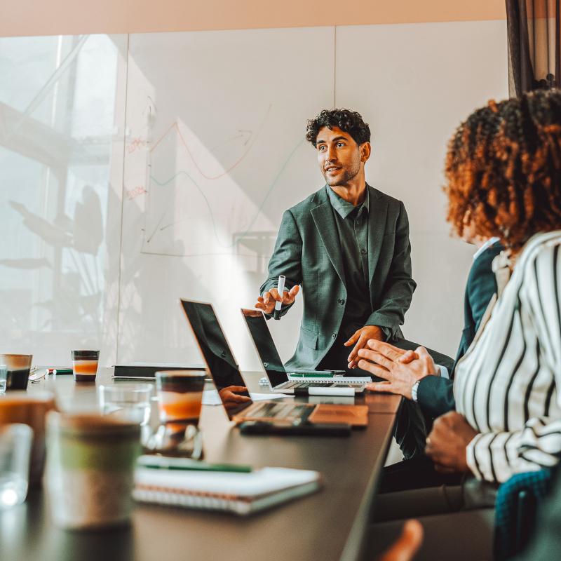 Man presents to co workers in meeting room 800