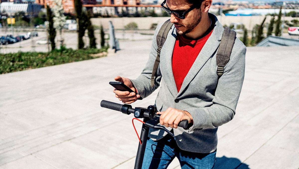 Man riding an e step looks at mobile phone Man riding an e step looks at mobile phone