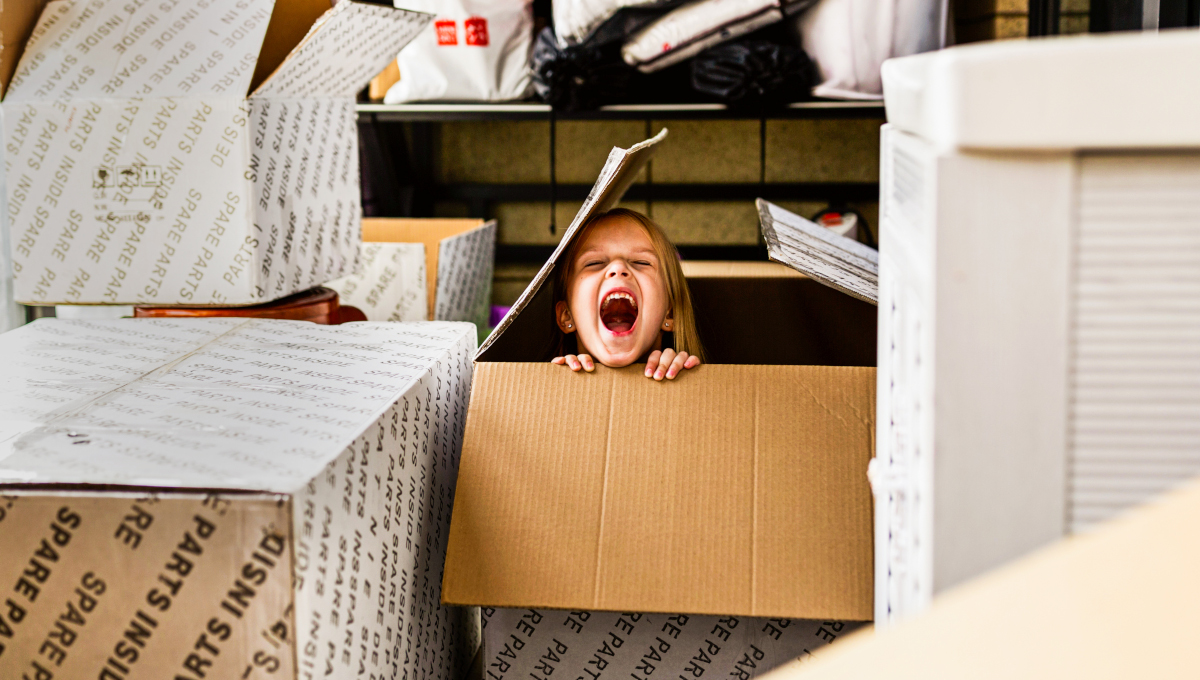 small child laughing as they hide in a cardboard box indoors 1200