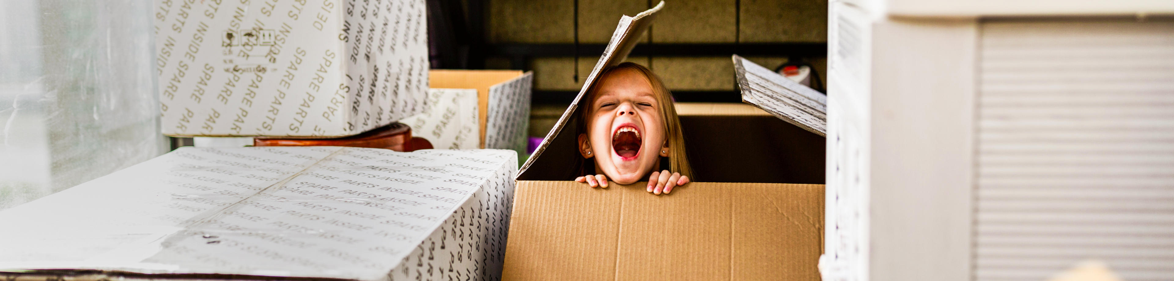 Small child laughing as they hide in a cardboard box indoors large