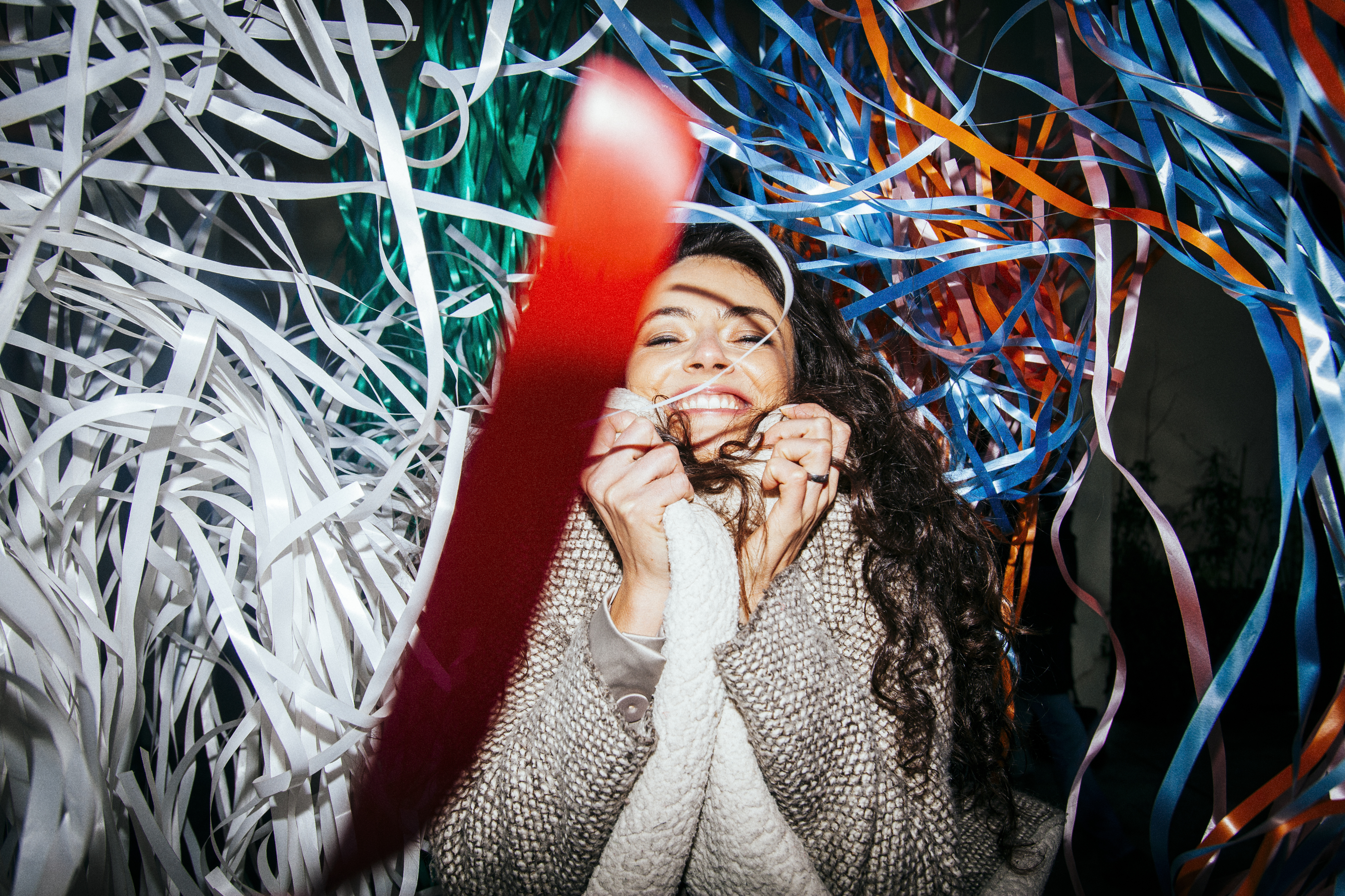 Young woman with long hair wraps coat around herself and smiles in the middle of some paper streamers